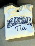 White sweatshirt with blue floral applique GRANDMA letters and the name Tia embroidered in navy script