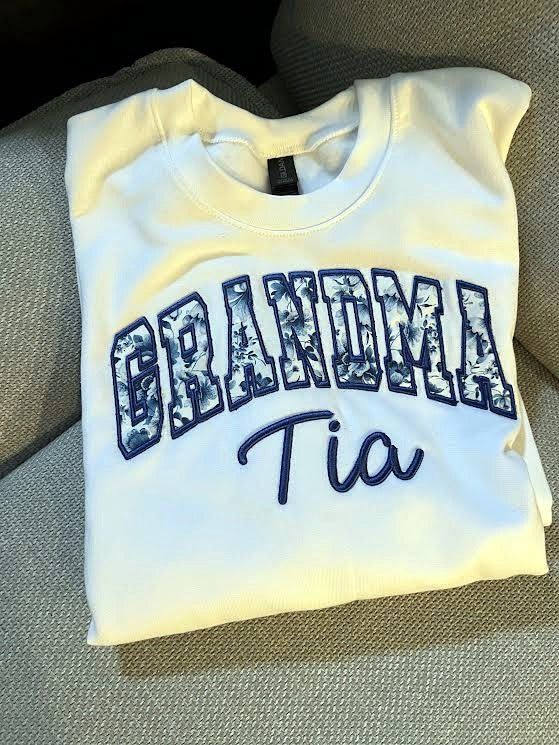 White sweatshirt with blue floral applique GRANDMA letters and the name Tia embroidered in navy script